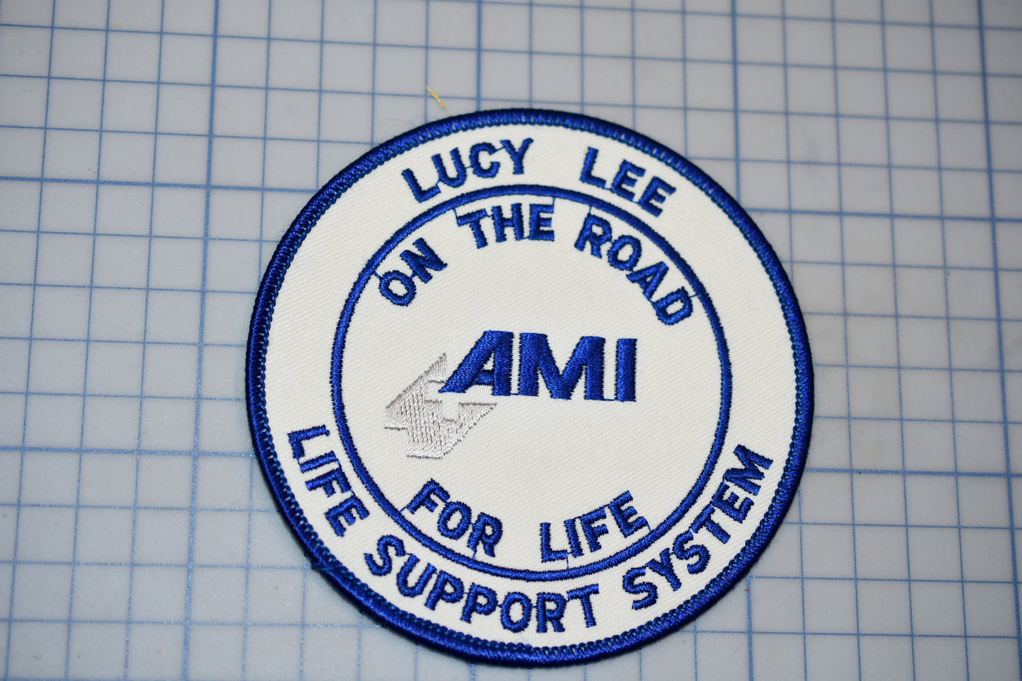 a circular patch with the text "LUCY LEE ON THE ROAD AMI LIFE SUPPORT SYSTEM" embroidered on it.