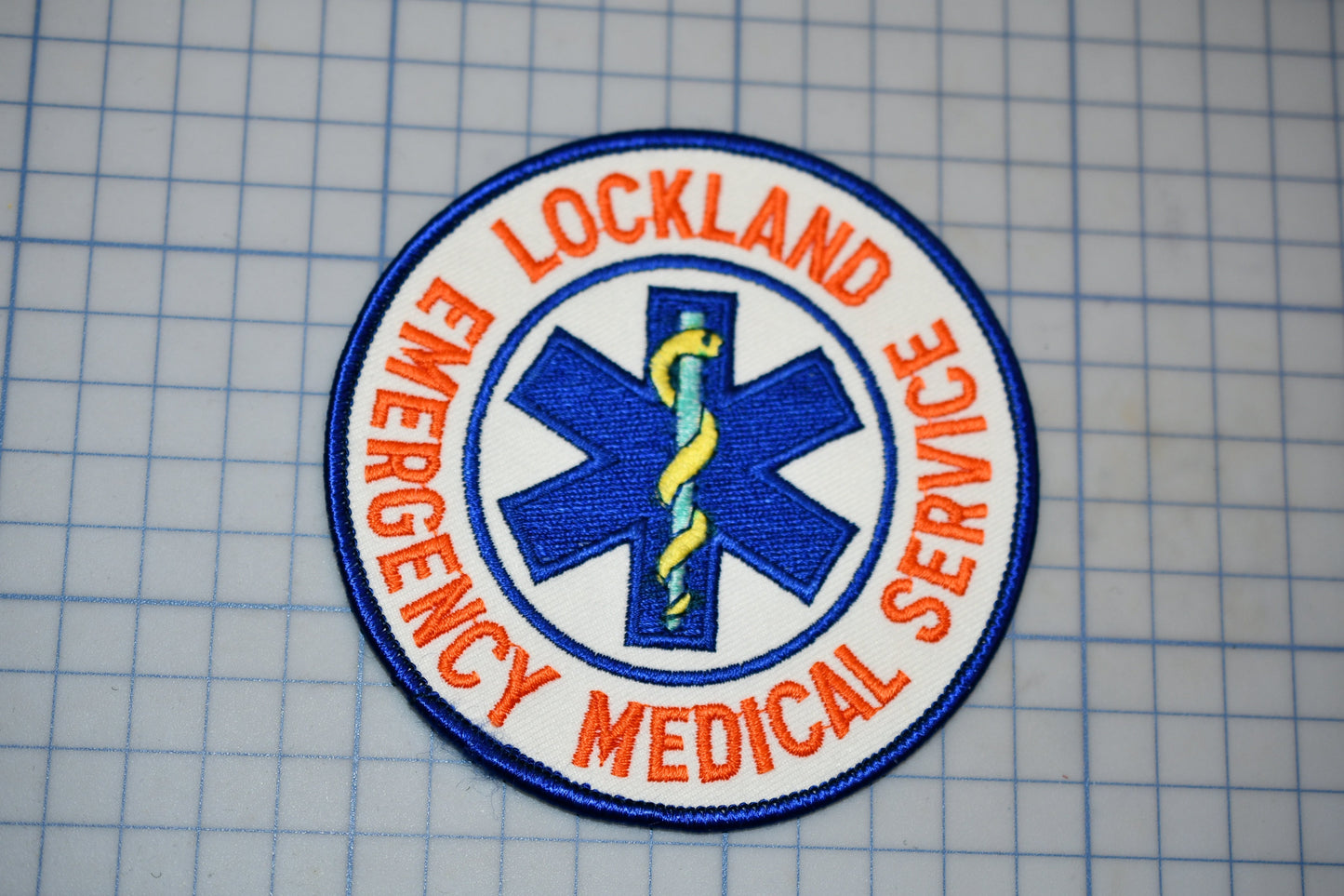 a circular patch with the text "LOCKLAND EMERGENCY MEDICAL SERVICE" and a medical symbol, such as a cross or stethoscope, encircling it.