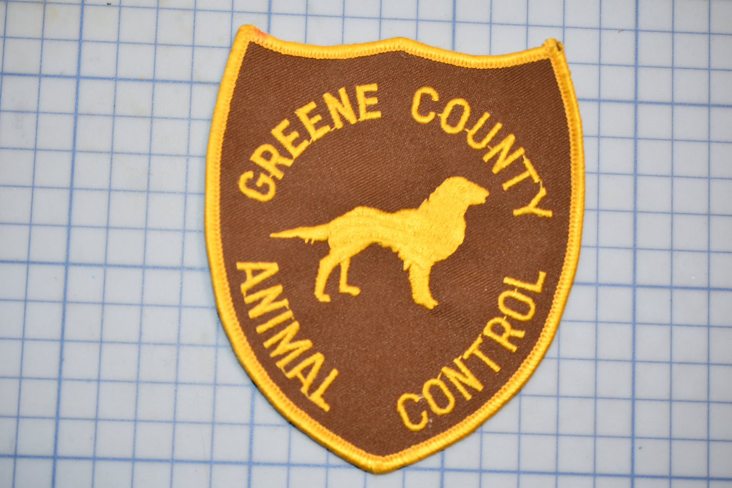 A brown and yellow patch with the text "GREENE COUNTY ANIMAL CONTROL" and a silhouette of a dog.