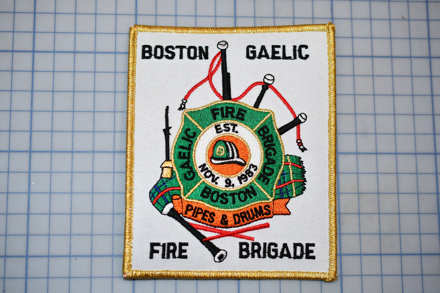 a patch with a fire department emblem, including a fire engine, a fire hose, and a fire helmet, along with the text "Fire Brigade" and "Pipes & Drums".