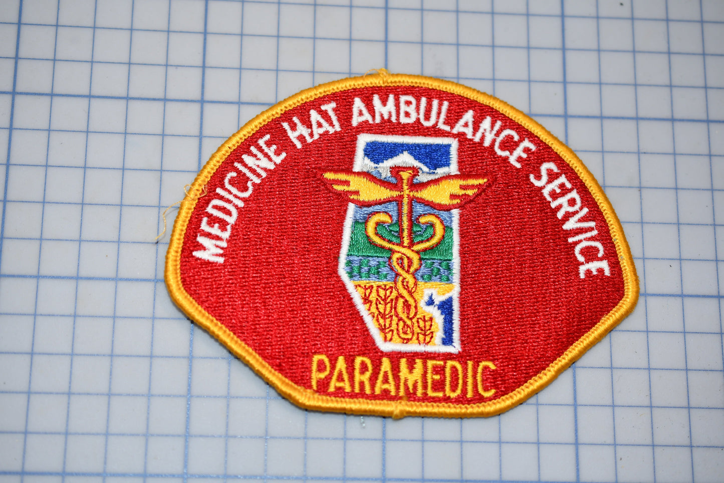 a red and yellow patch with the word "PARAMEDIC" written on it, along with a medical symbol and the word "MEDICINE HAT AMBULANCE SERVICE" written around it.