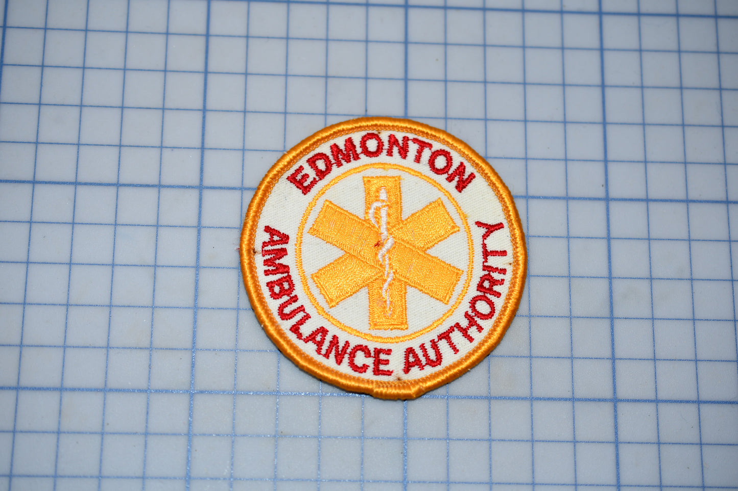a patch with the text "EDMONTON AMBULANCE AUTHORITY" and a symbol of a cross, which is a common emblem associated with emergency medical services.