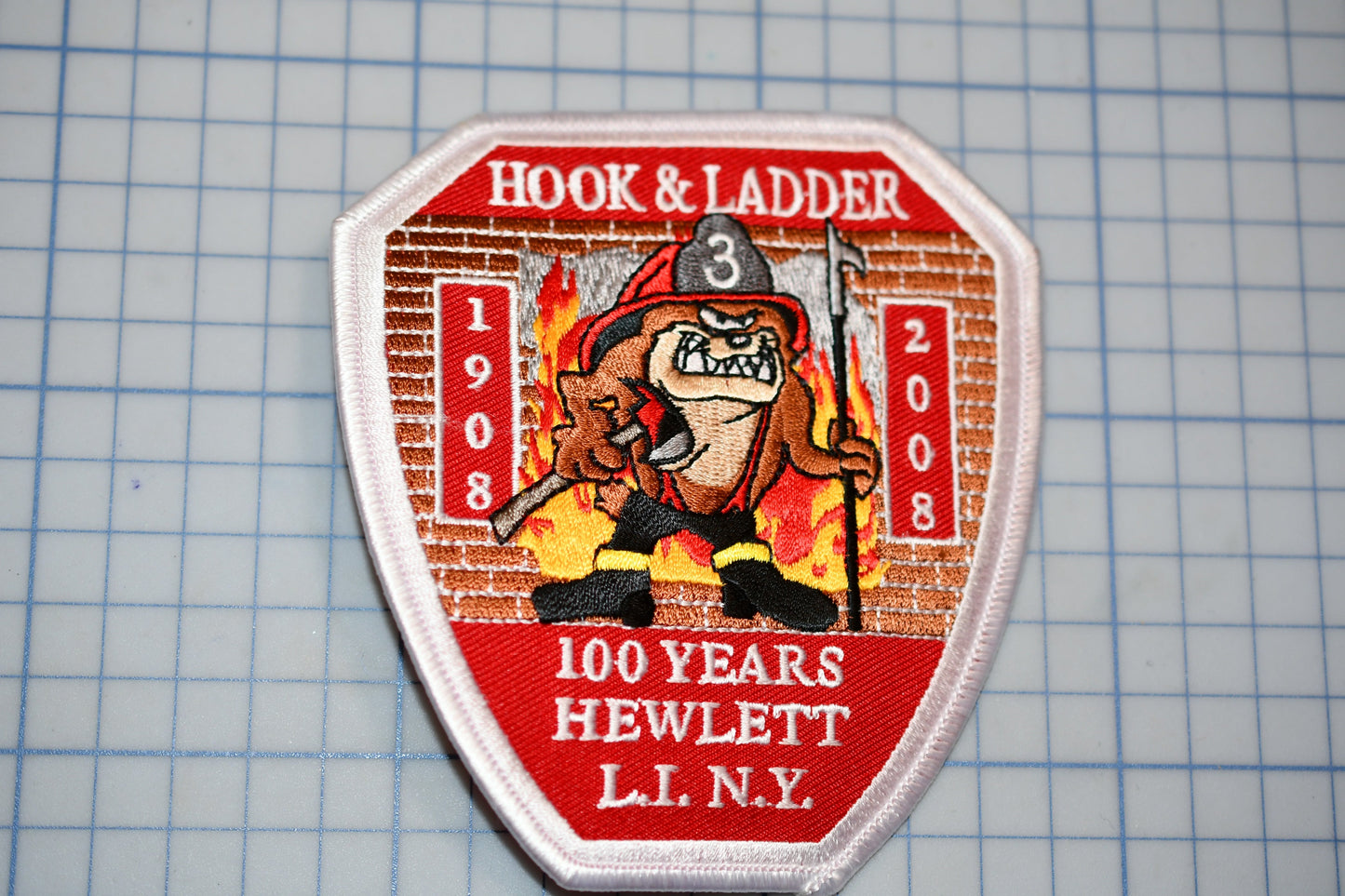 a patch with a cartoon fireman and the text "HOOK & LADDER" and "100 YEARS HEWLETT LI. NY".