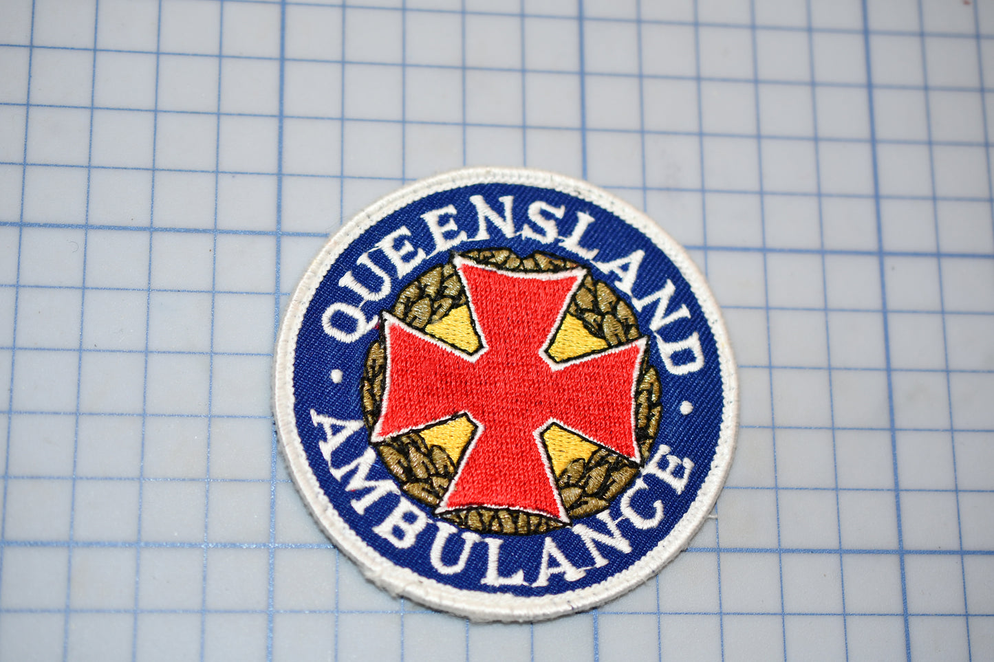 a circular patch with a red cross and the text "Queensland Ambulance" written around it.