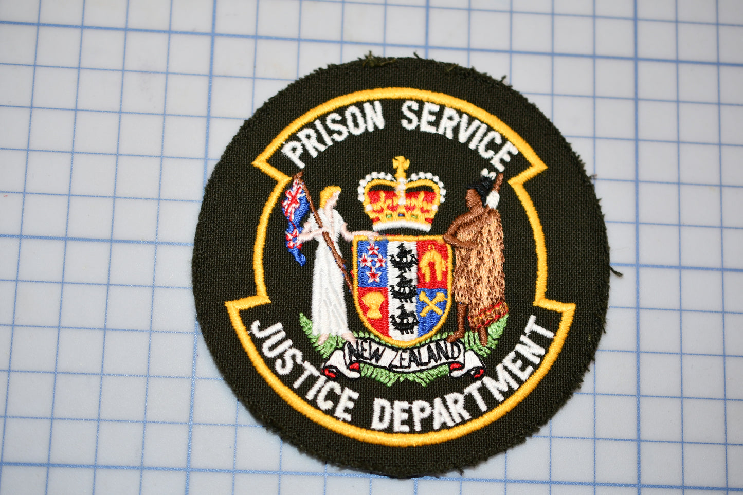 a circular emblem with text and a coat of arms, which appears to be a symbol or insignia associated with the Prison Service Justice Department.