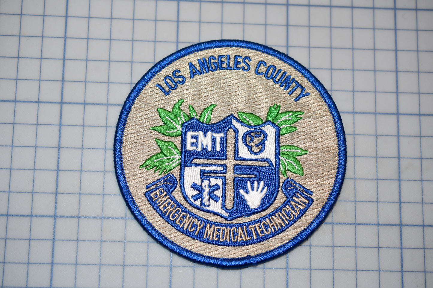 a badge or patch with the text "Los Angeles County EMT Emergency Medical Technician" and a shield-like emblem with a cross and leaves.