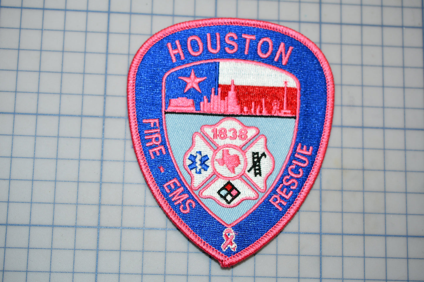 A patch with the text "HOUSTON FIRE - EMERGENCY RESCUE" and a shield-shaped emblem featuring a city skyline, a fireman's helmet, and a ribbon symbol.
