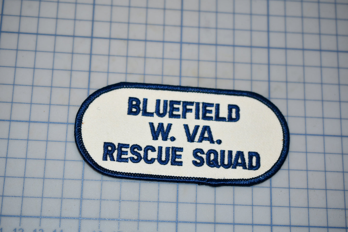 A patch with the text "BLUETFIELD W. VA. RESCUE SQUAD" printed on it, indicating that it is a patch from the Bluefield Rescue Squad.