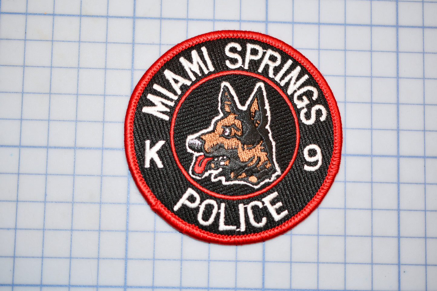 A red and black patch with a dog's head and the text "MIAIM SPRINGS POLICE" printed on it.