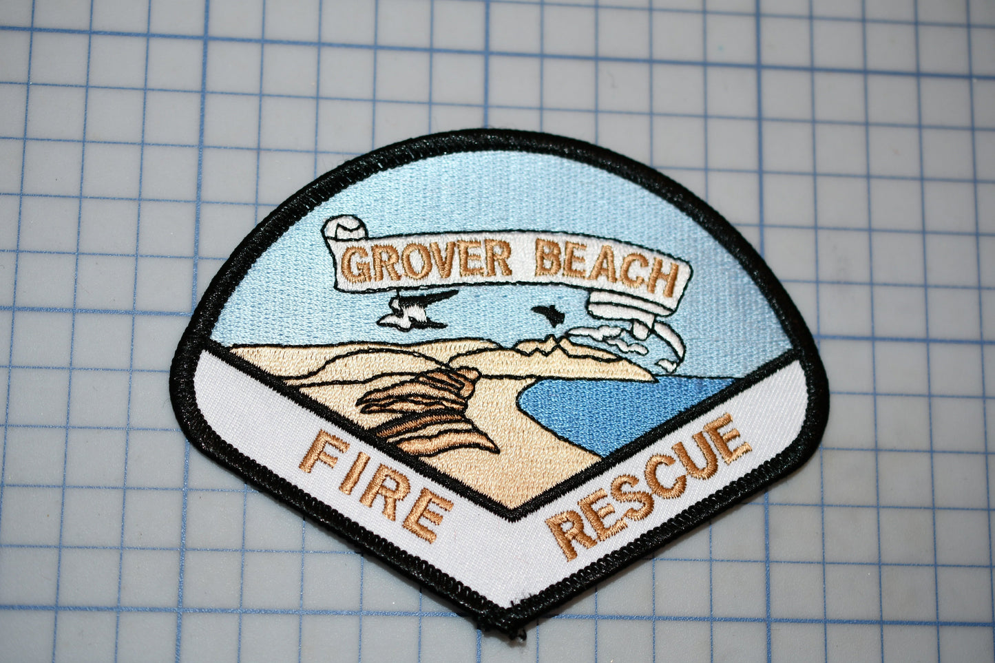 a patch with the text "GROVER BEACH FIRE RESCUE" and an illustration of a beach scene with mountains, a bird, and a body of water.
