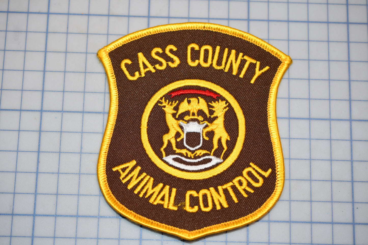 A brown and gold patch with the text "CASS COUNTY ANIMAL CONTROL" and a coat of arms, indicating the presence of an animal control service.
