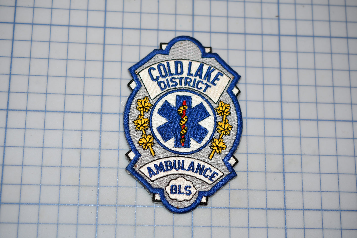 a badge or patch with the text "COLD LAKE DISTRICT AMBULANCE" and a medical symbol, indicating that it is a badge or patch from the Cold Lake District Ambulance.