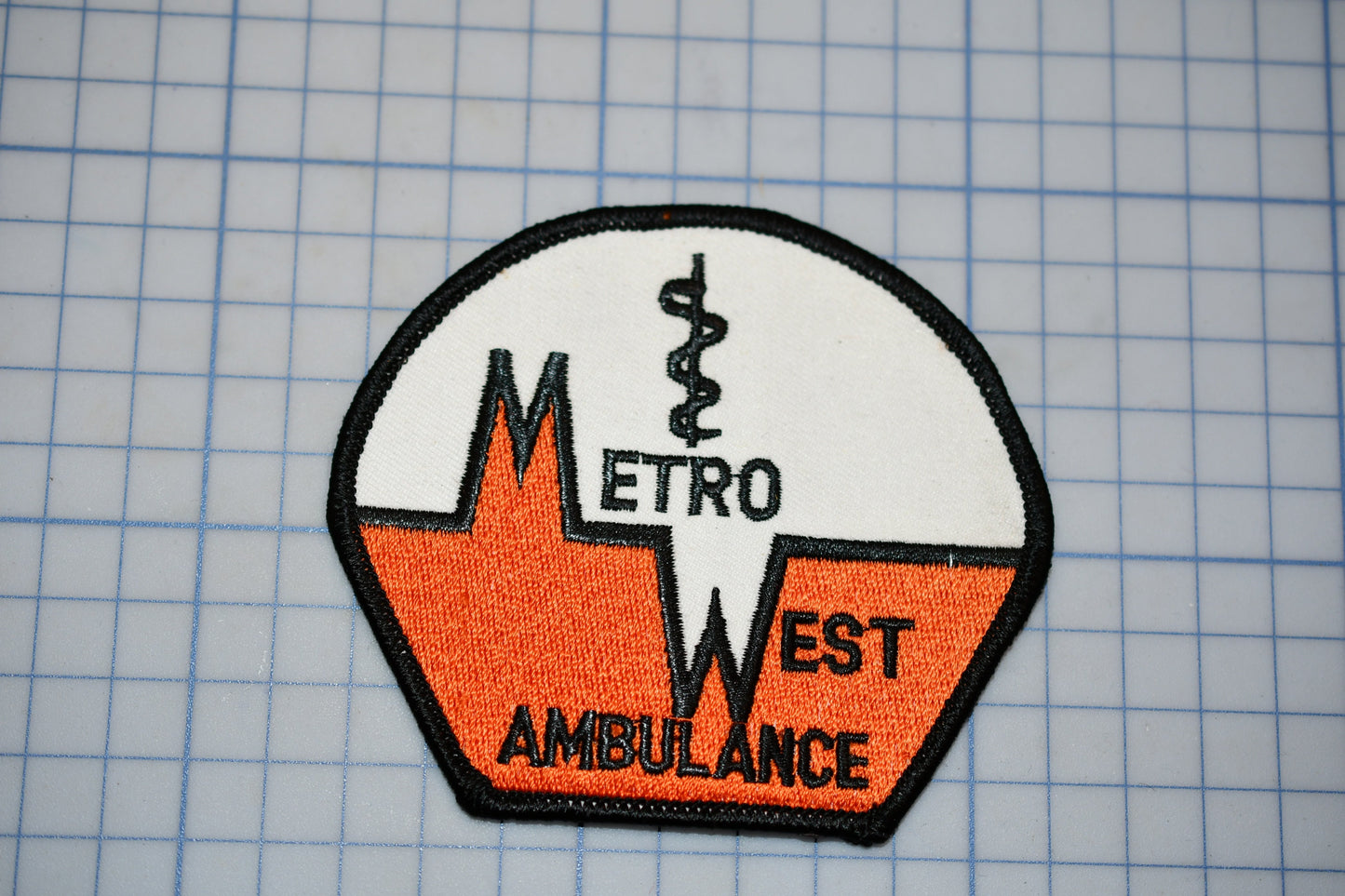 a patch with the text "METRO WEST AMBULANCE" and a medical symbol, likely representing an emergency medical service.