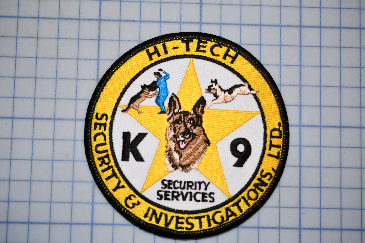 a circular patch with a yellow border, containing an embroidered design and text.