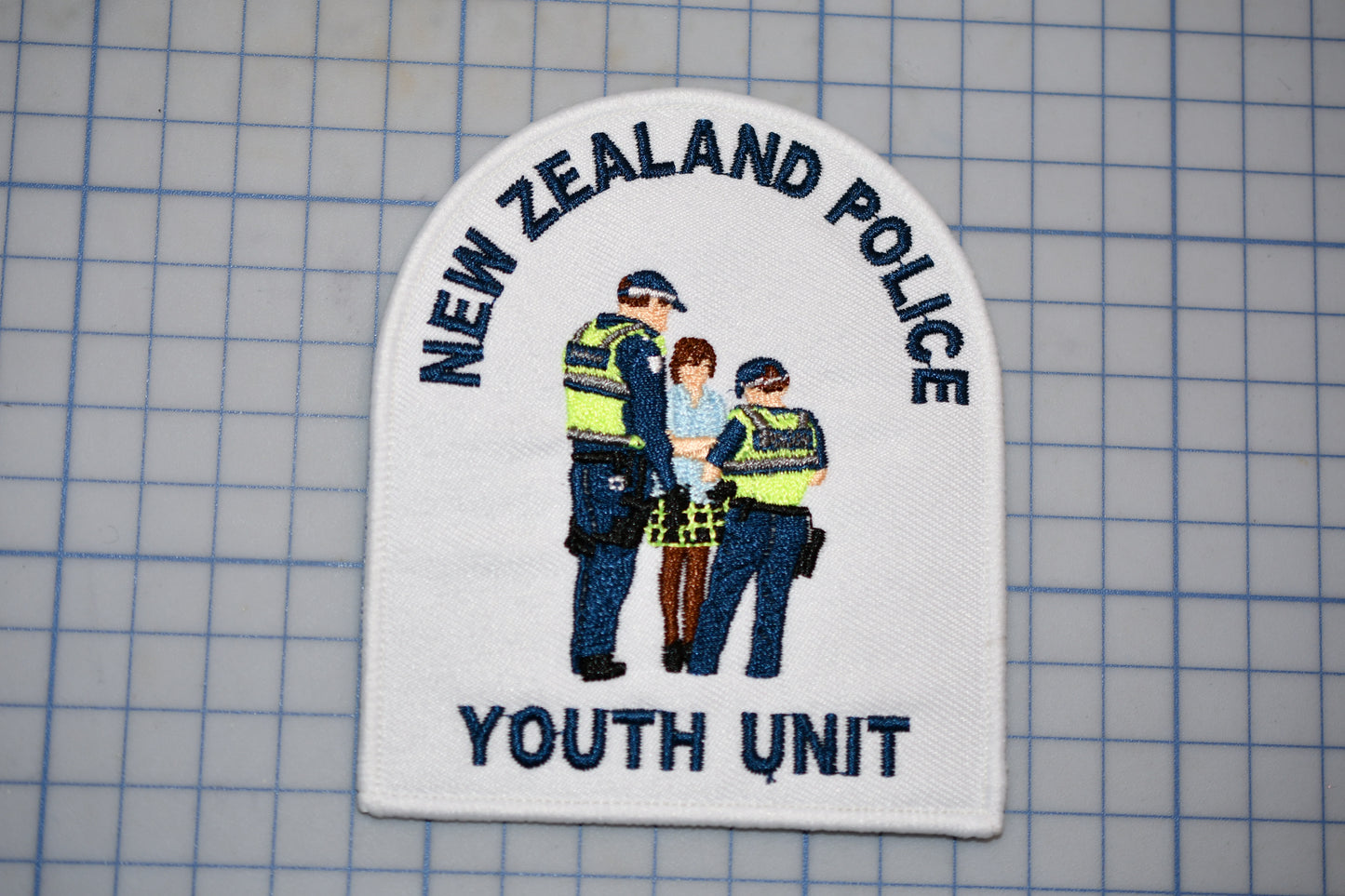 a patch with the text "NEW ZEALAND POLICE Youth Unit" and an illustration of three police officers.