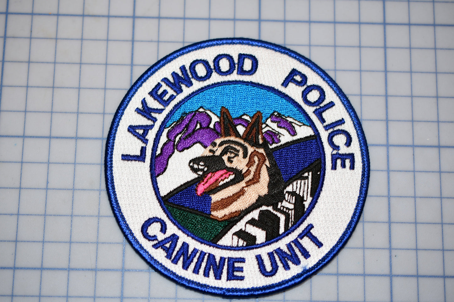 a badge or patch with a dog and mountains in the background, surrounded by the text "LAKEWOOD POLICE CANINE UNIT".