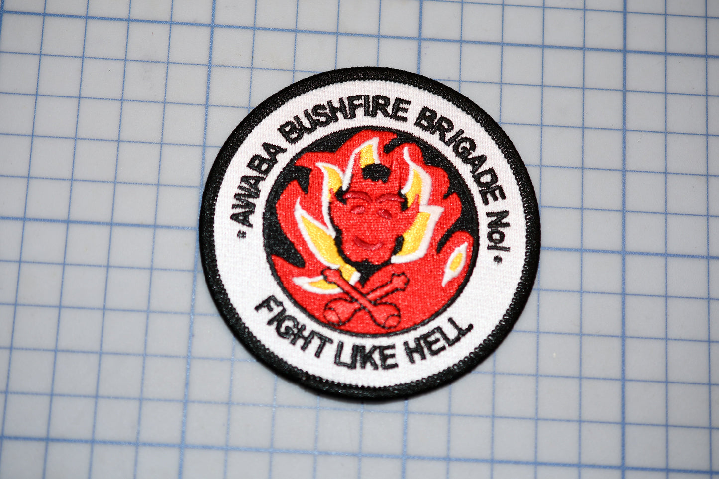 a circular patch with a red devil-like figure and flames, surrounded by the text "ANNABAA BUSHFIRE BRIGADE No.1 - FIGHT LIKE HELL".