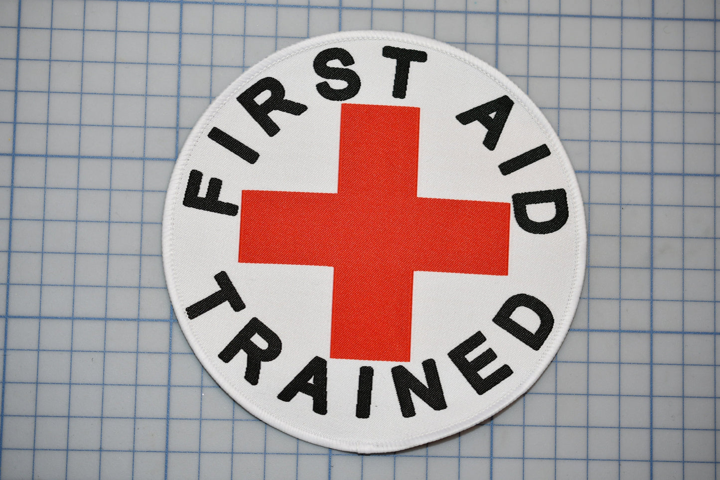 A white circle with a red cross and the text "FIRST AID TRAINED" printed on it.