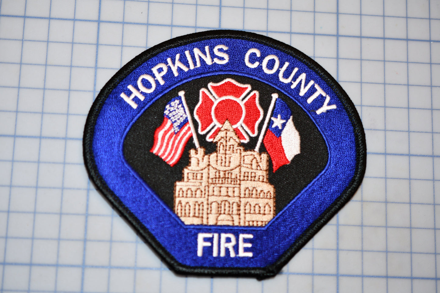 A blue and black patch with the text "HOPKINS COUNTY FIRE" and an illustration of a building with a fire hydrant and fire truck.