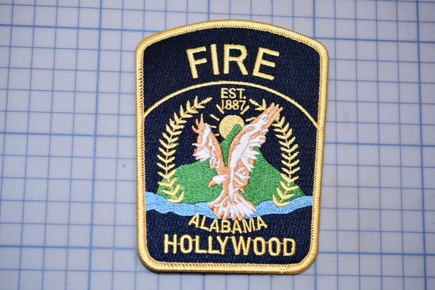 a fire department patch with the text "FIRE EST. 1987 ALABAMA HOLLYWOOD" and an eagle emblem.