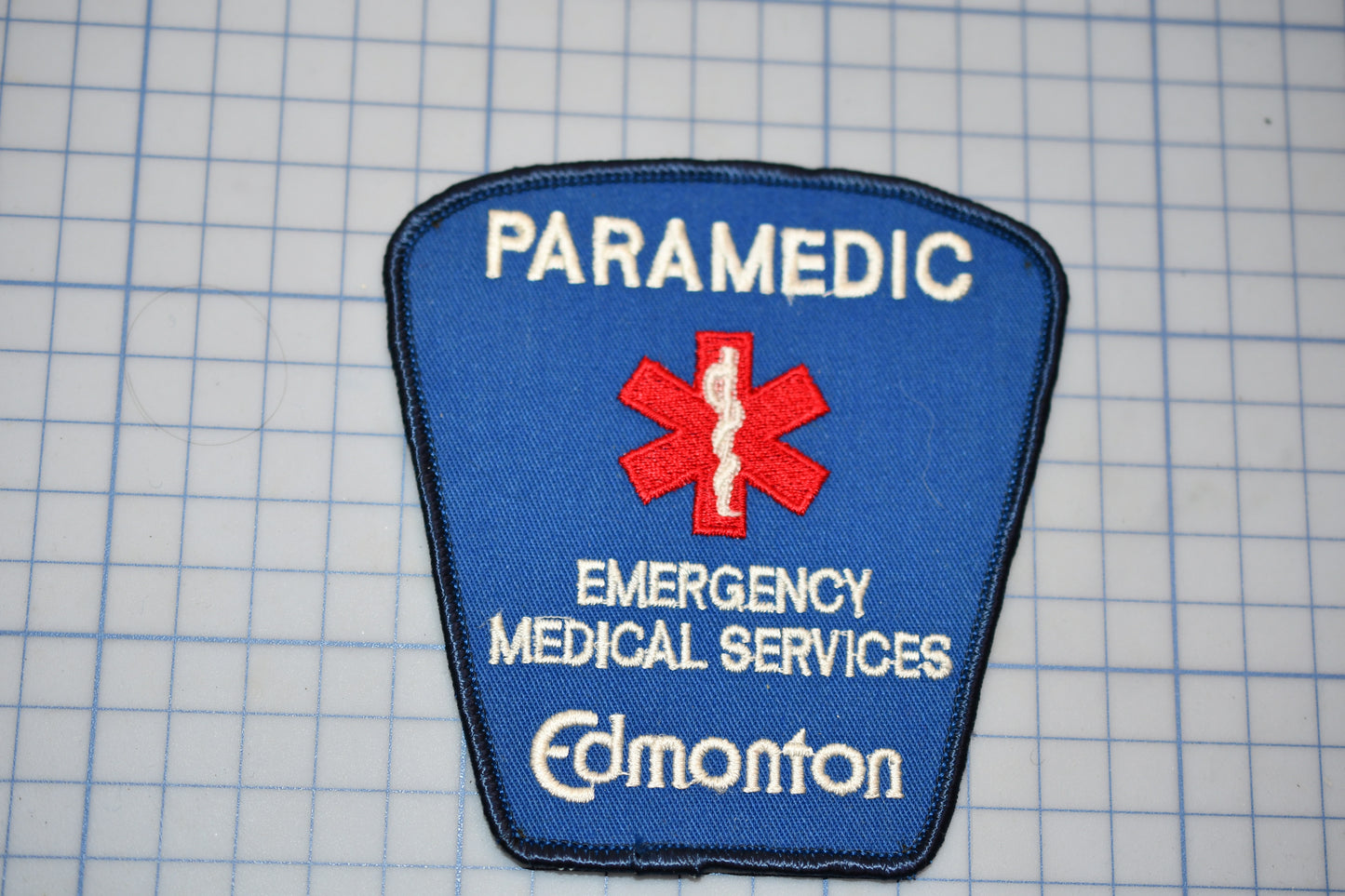 A blue emergency medical services patch with the word "PARAMEDIC" and the word "EMERGENCY MEDICAL SERVICES" printed on it, along with a red cross symbol.