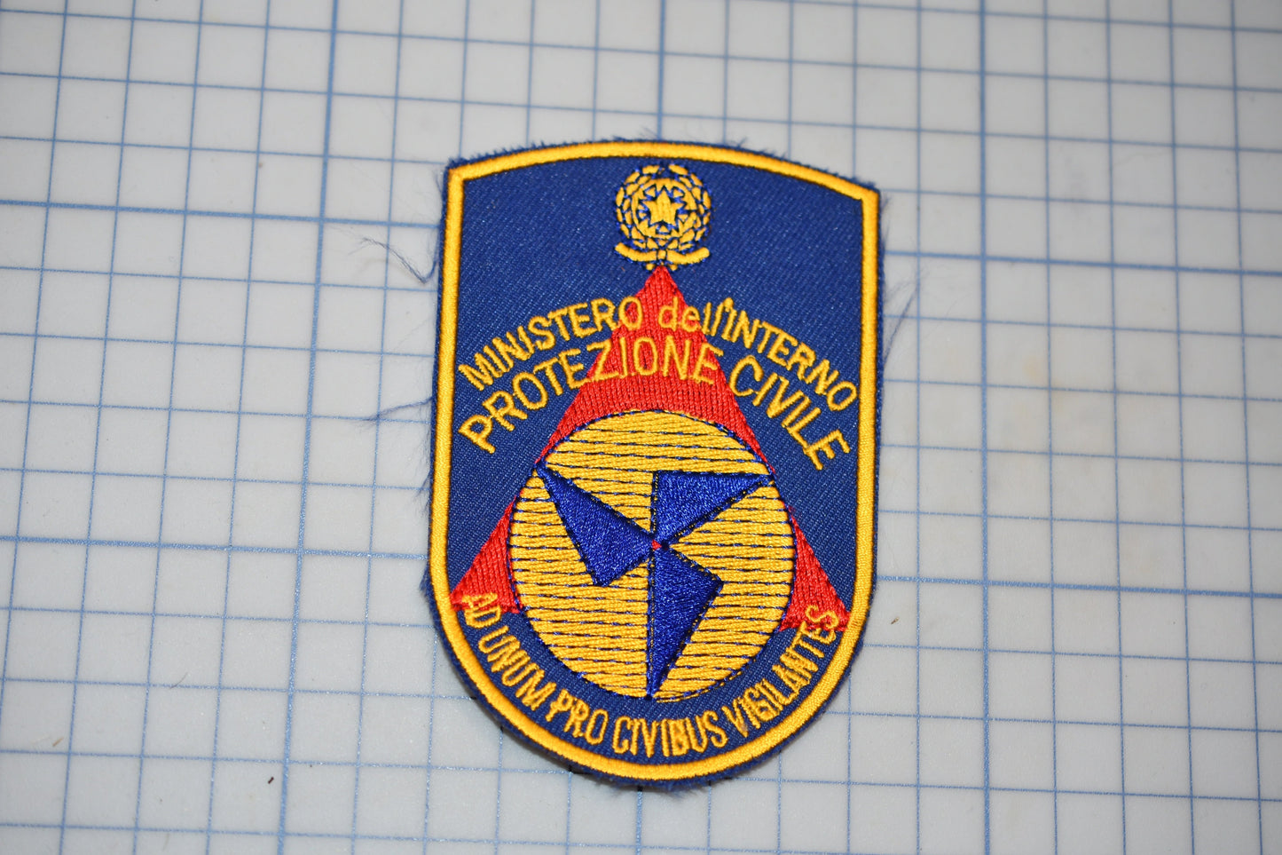 a blue and yellow patch with text and a symbol, placed on a grid background.