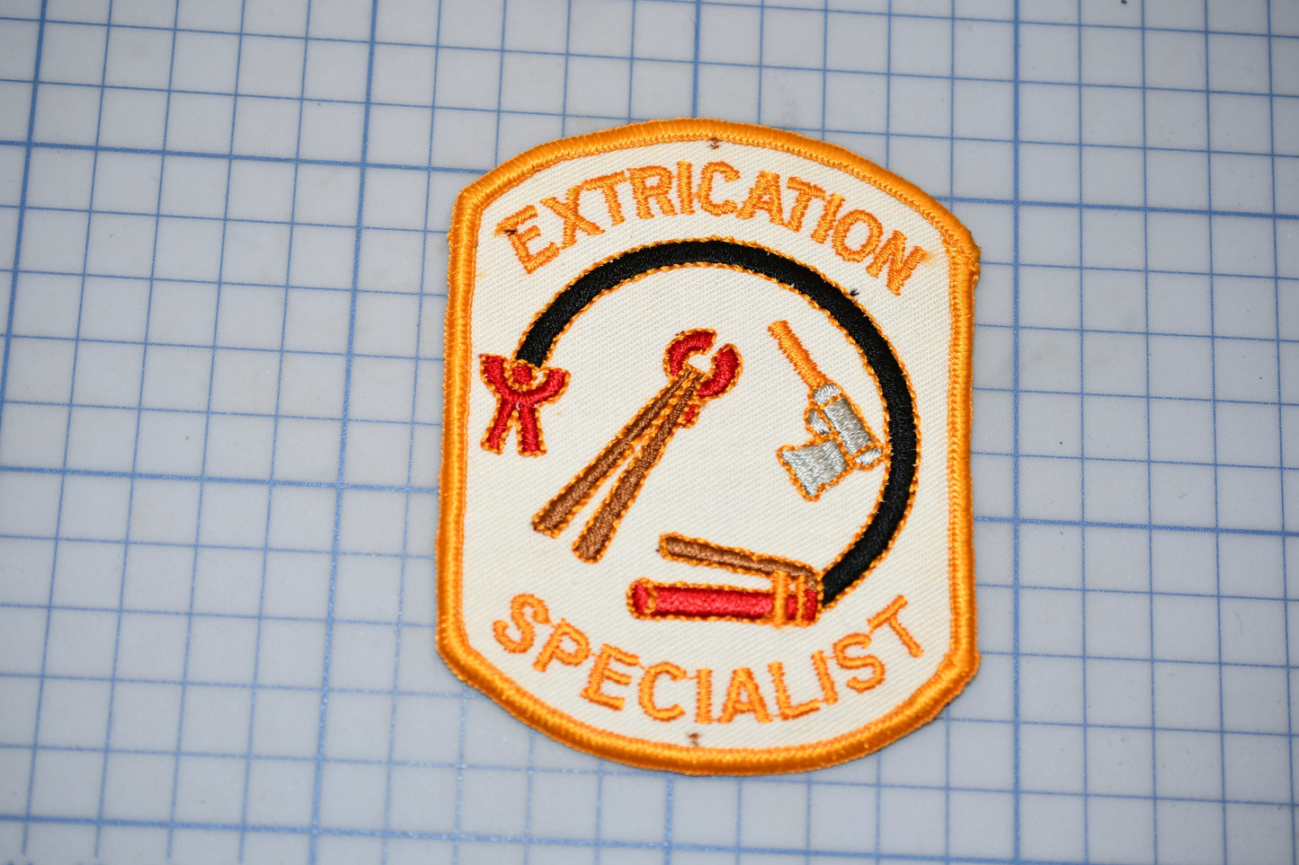 a patch with the text "EXTRICATION SPECIALIST" and various tools, such as a wrench and pliers, arranged around a central figure.