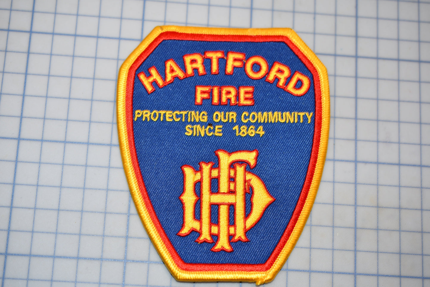 A blue and gold fire department patch with the text "HARTFORD FIRE" and "PROTECTING OUR COMMUNITY SINCE 1864" printed on it.