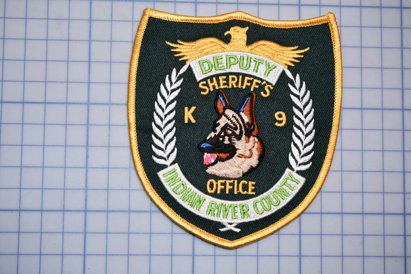a badge with the text "DEPUTY SHERIFF'S K-9 INDIAN RIVER COUNTY" and an embroidered image of a German Shepherd dog.