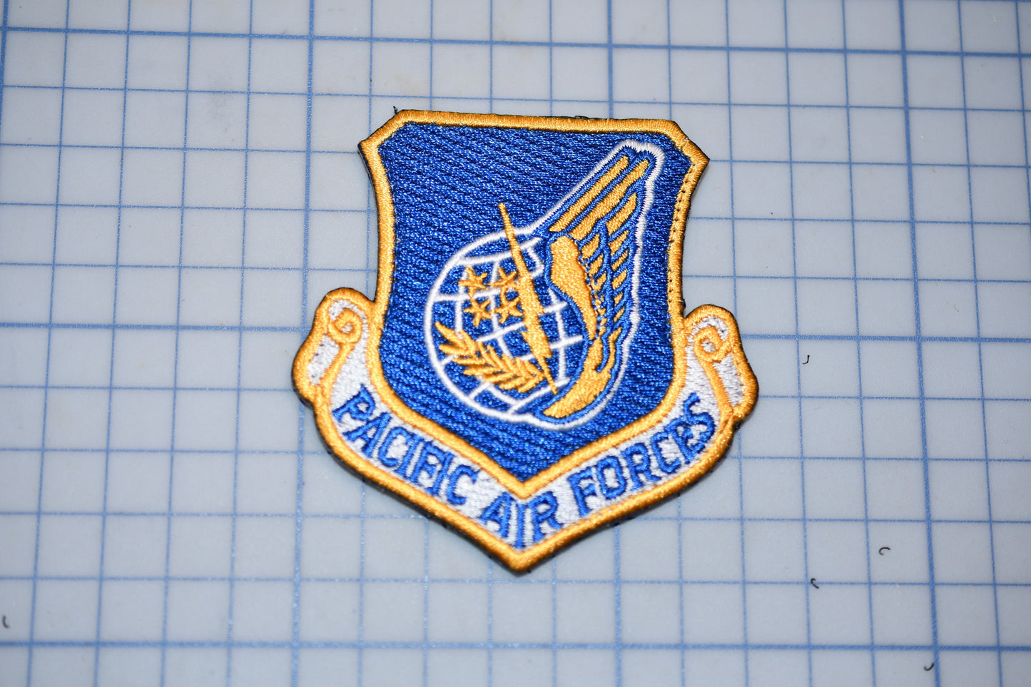 a blue and gold patch with the text "PACIFIC AIR FORCES" on it, which appears to be a military or service insignia.