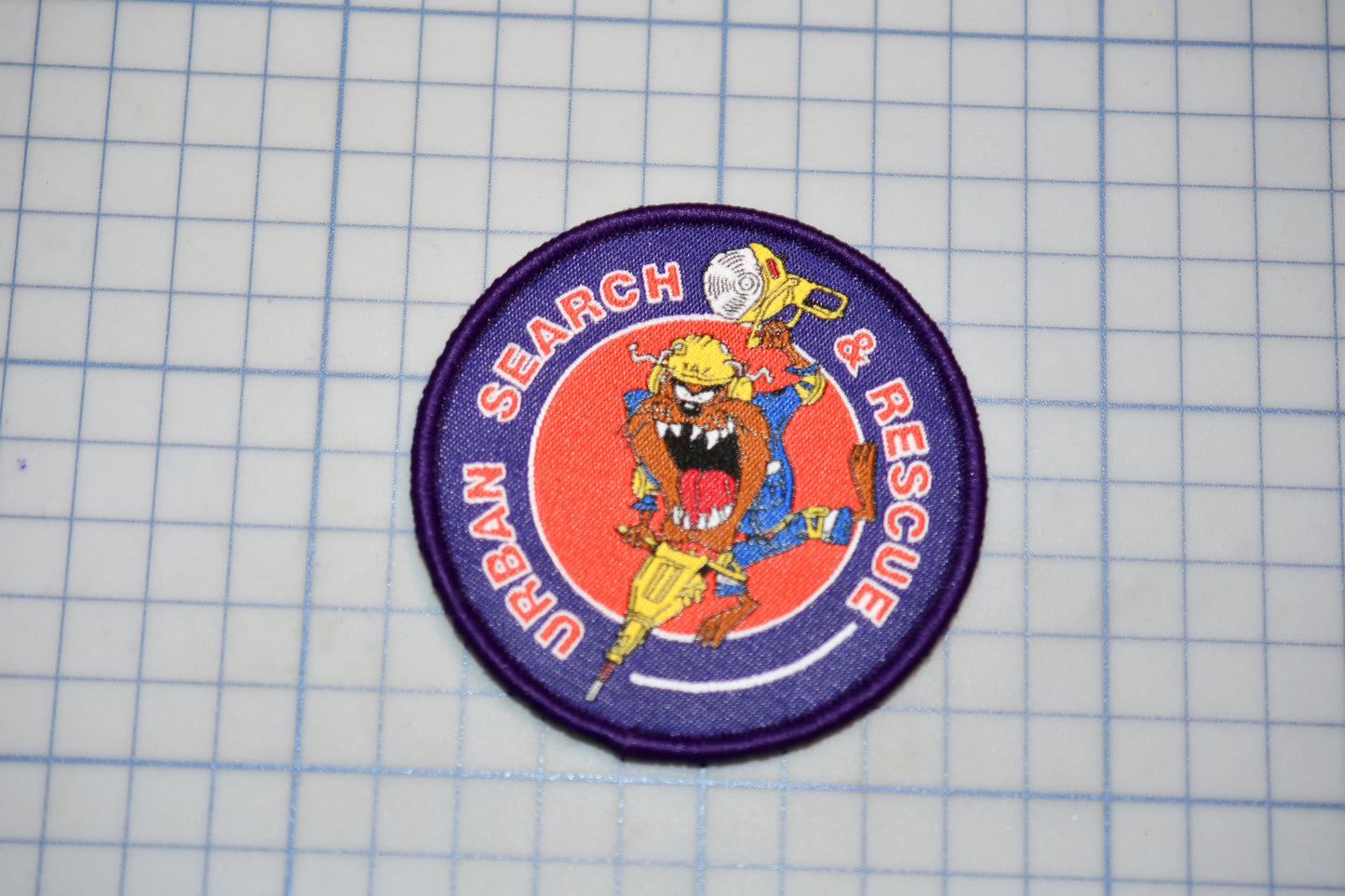a circular patch with a cartoon character and the text "Search & Rescue" on it, placed on a grid background.