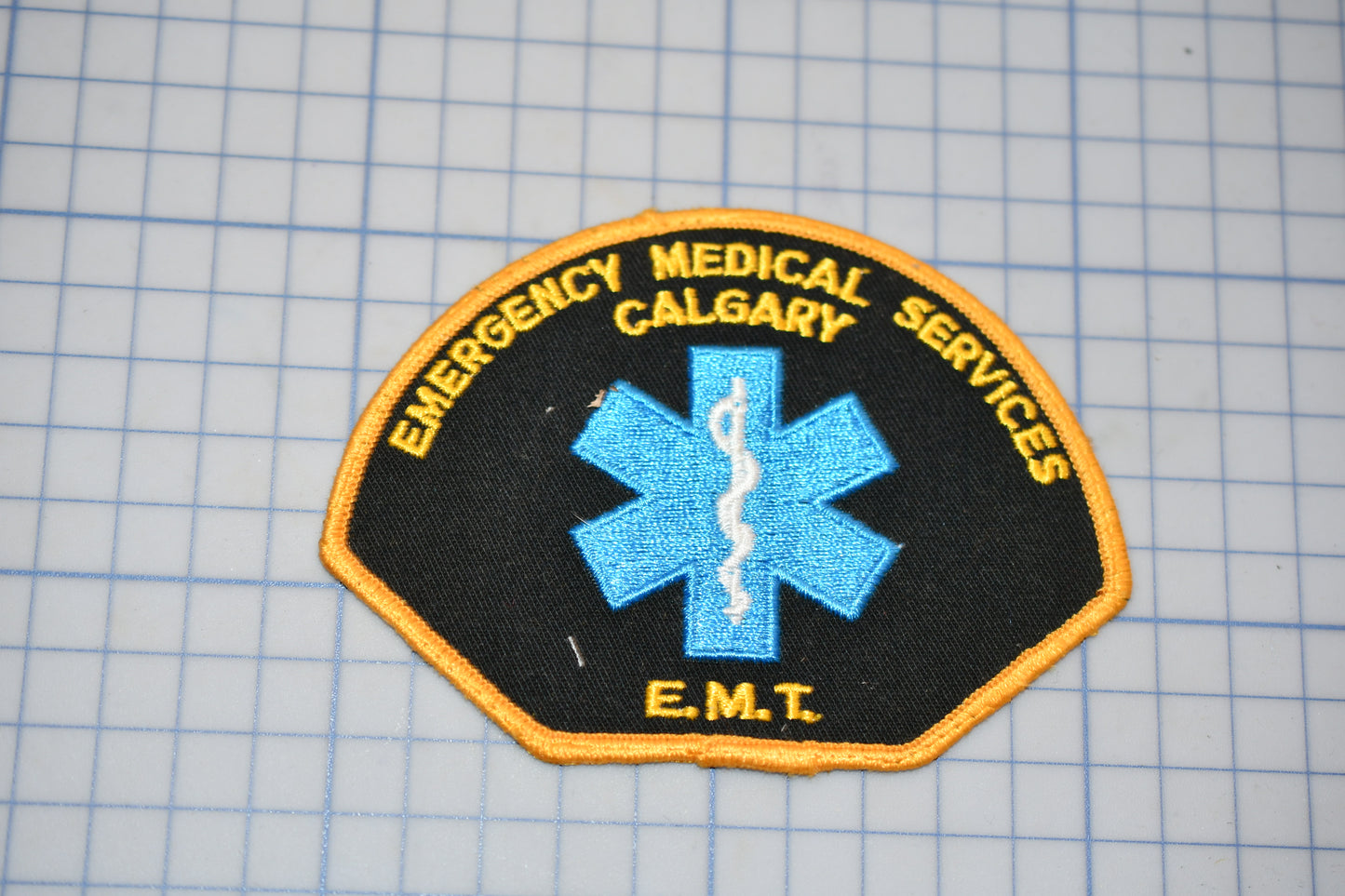 a patch with the text "EMT" and a blue medical symbol, indicating it is a patch from Emergency Medical Services.