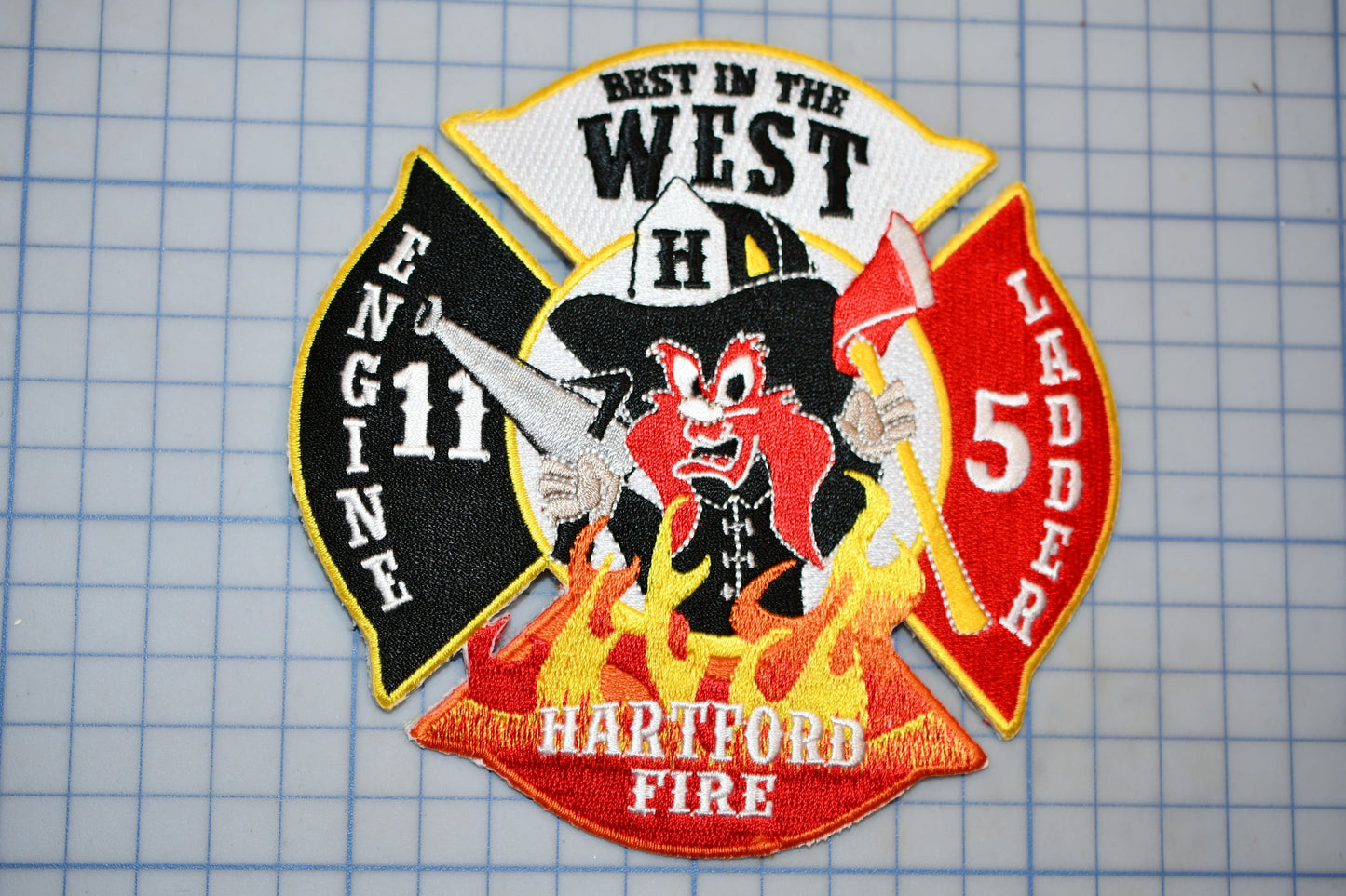 A fire department patch with a cartoon firefighter character, surrounded by flames and text indicating the department's name and location.