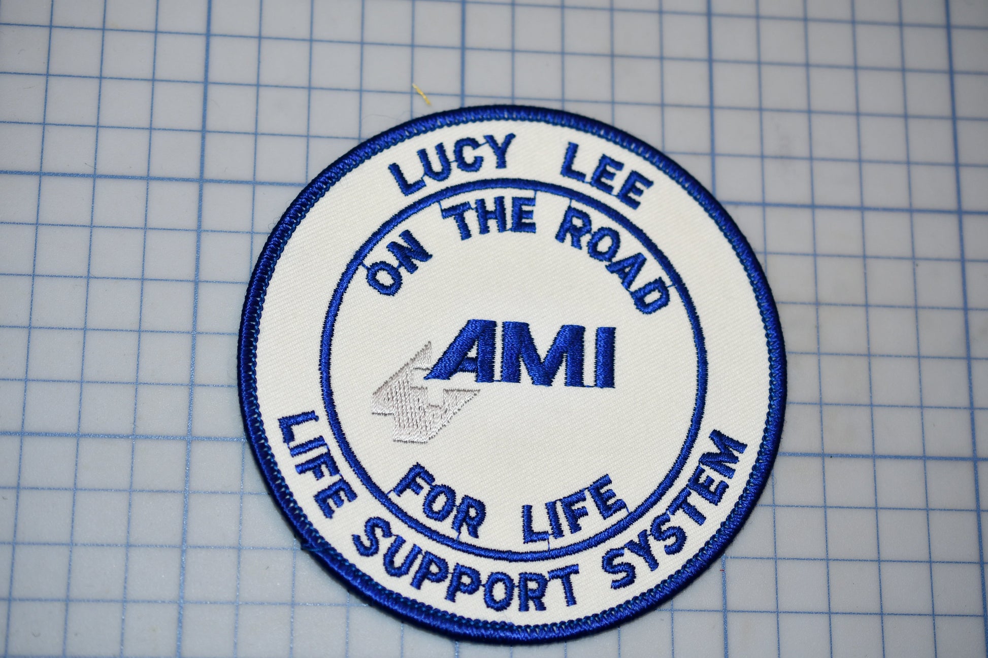 a circular patch with the text "LUCY LEE ON THE ROAD AMI LIFE SUPPORT SYSTEM" embroidered on it.