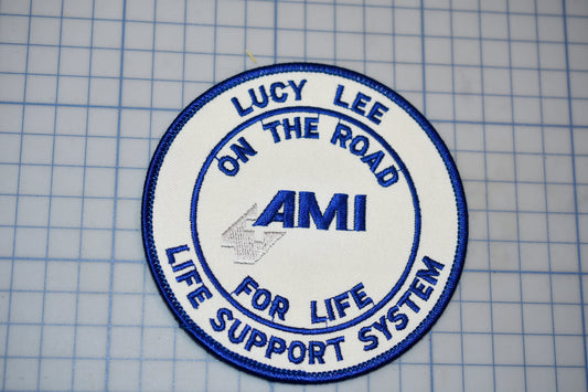 a circular patch with the text "LUCY LEE ON THE ROAD AMI LIFE SUPPORT SYSTEM" embroidered on it.
