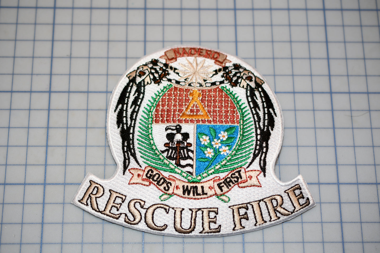 A patch with a coat of arms and the text "RESCUE FIRE" on it, placed on a grid background.