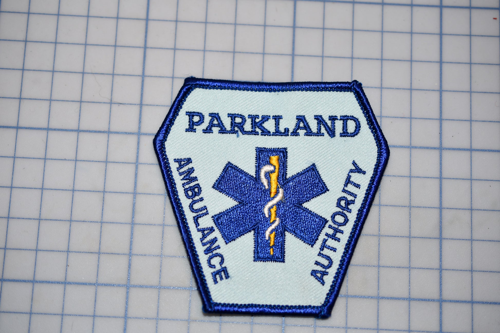 A badge with the text "PARKLAND AMBULANCE AUTHORITY" and a medical symbol, indicating that it is a badge or emblem of the Parkland Ambulance Authority.