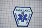 A badge with the text "PARKLAND AMBULANCE AUTHORITY" and a medical symbol, indicating that it is a badge or emblem of the Parkland Ambulance Authority.