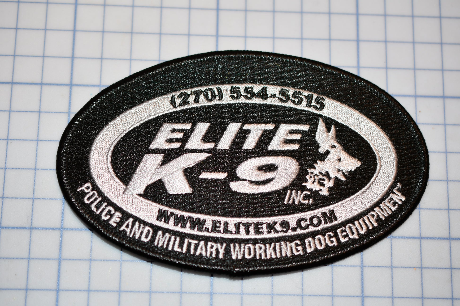 a black and white patch with text and logos, placed on a grid background.