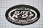 a black and white patch with text and logos, placed on a grid background.