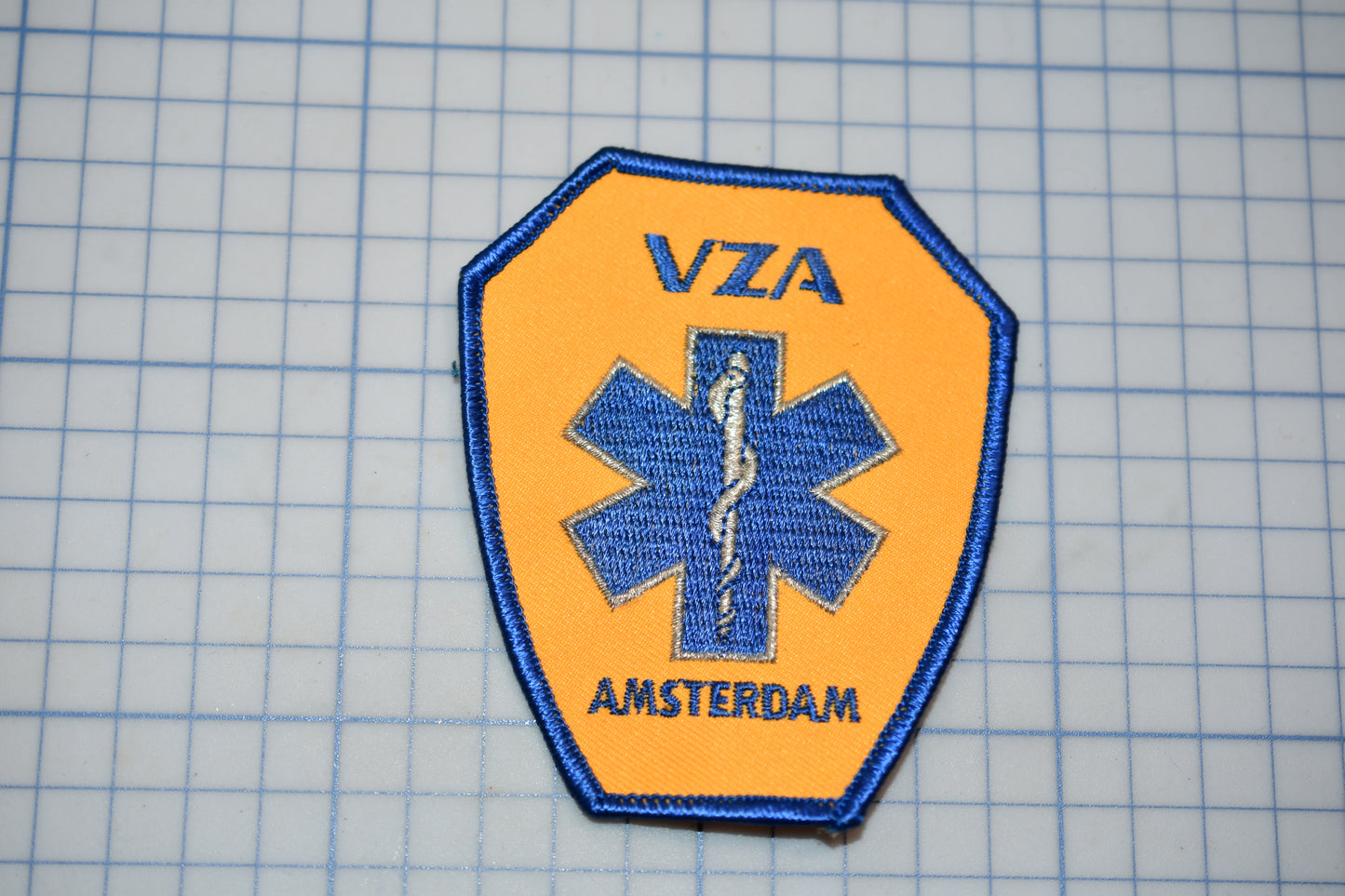 a medical patch with a blue cross symbol and the text "VZA AMSTERDAM" printed on it.