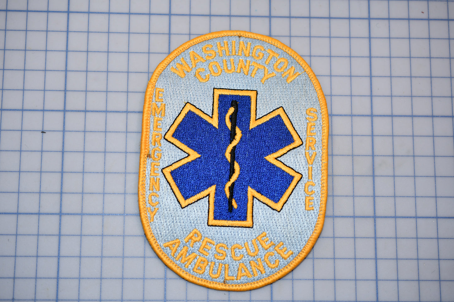 a patch with the text "WASHINGTON COUNTY EMERGENCY SERVICE RESCUE AMBULANCE" and a blue and yellow star-shaped symbol, which is commonly associated with emergency medical services.