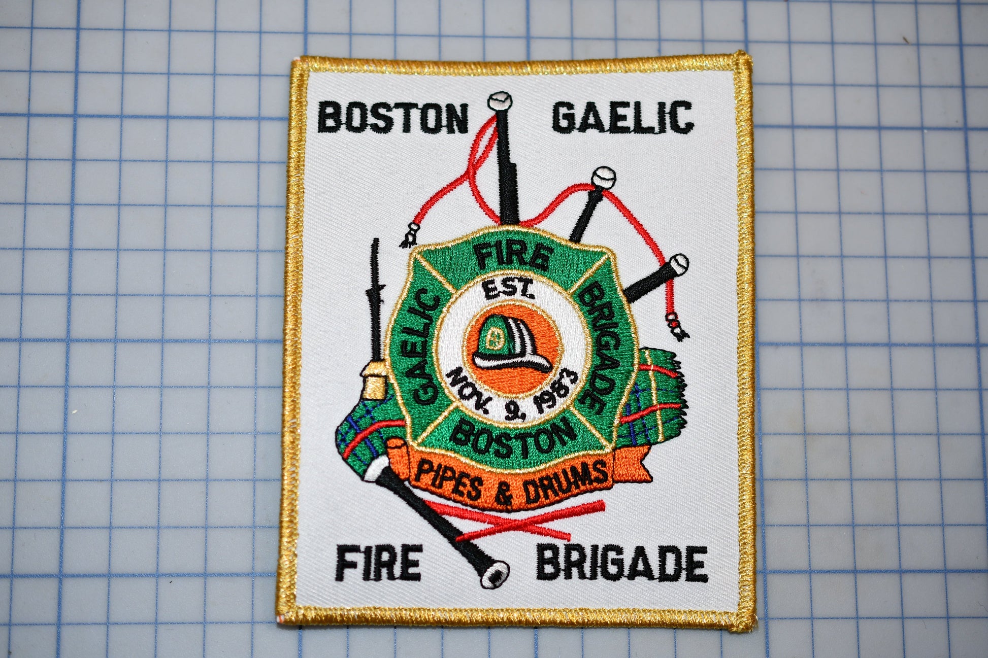 a patch with a fire department emblem, including a fire engine, a fire hose, and a fire helmet, along with the text "Fire Brigade" and "Pipes & Drums".