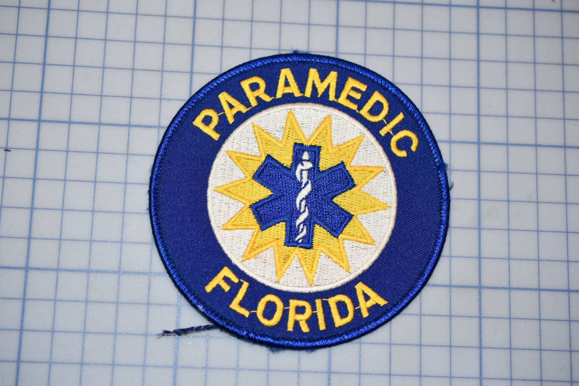 a blue and yellow patch with the text "PARAMEDIC FLORIDA" and a medical symbol, likely representing a medical emergency response team or organization.