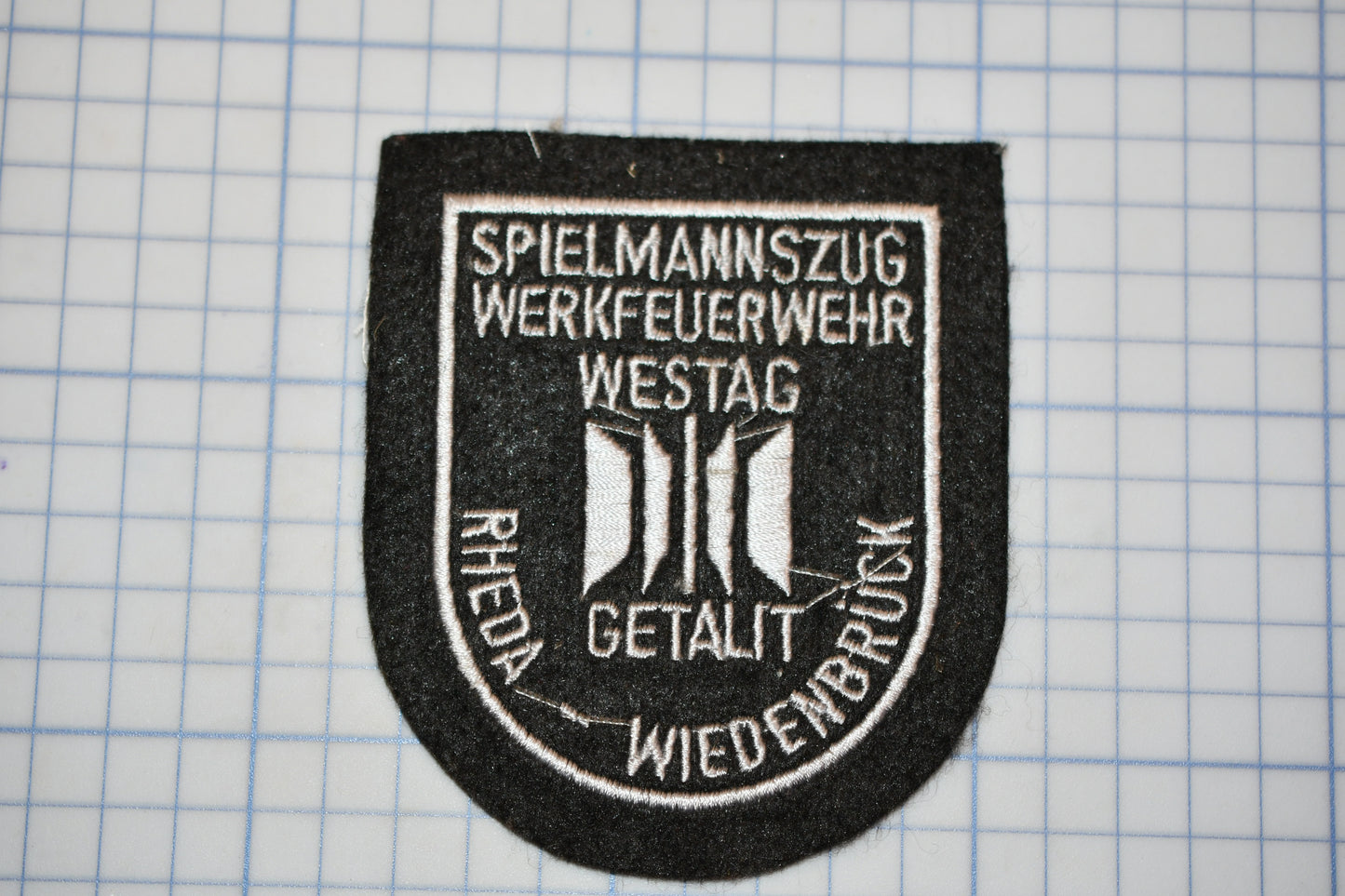 a black and white patch with text and symbols, placed on a grid background.
