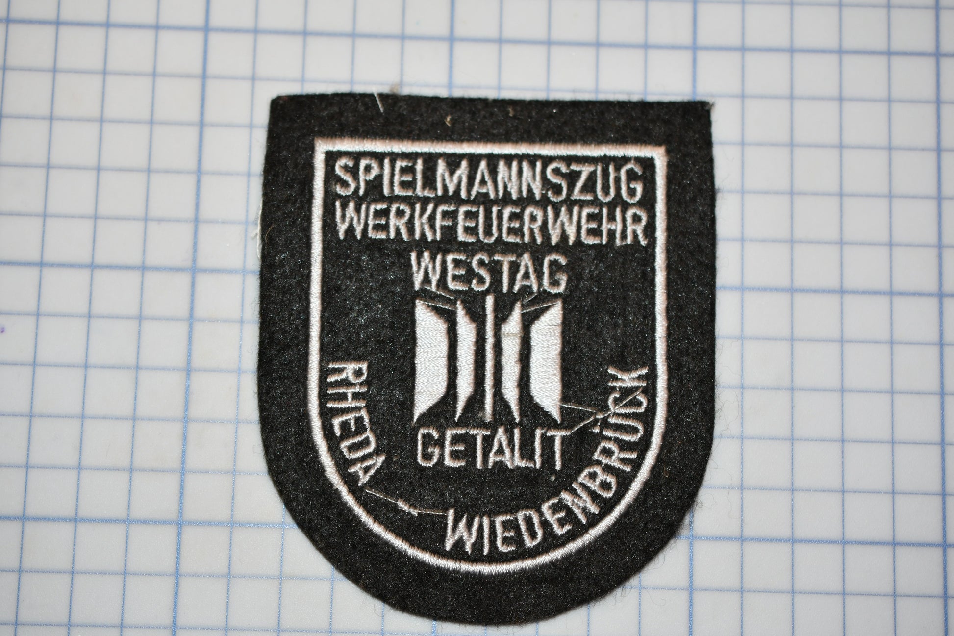 a black and white patch with text and symbols, placed on a grid background.