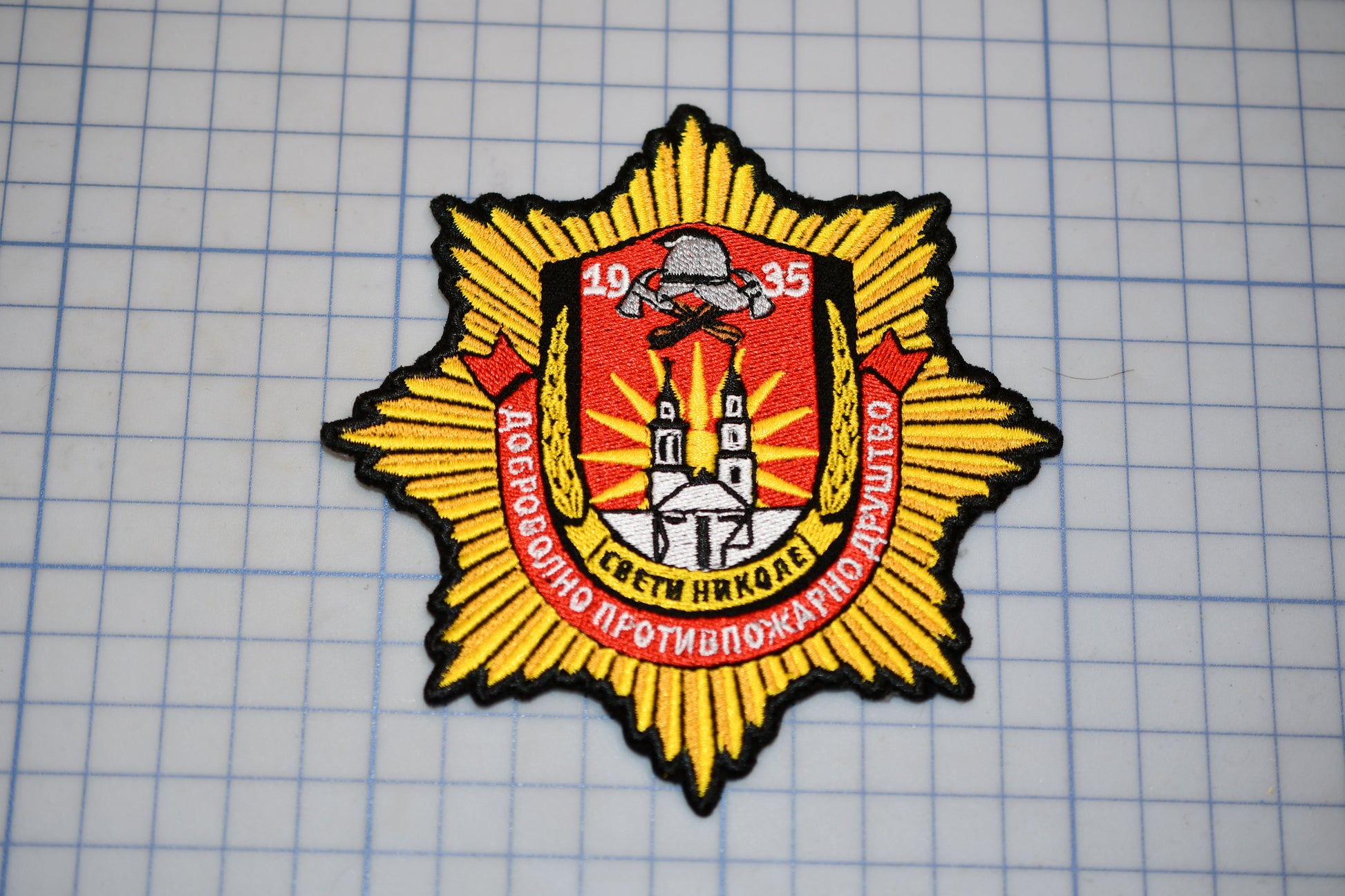 a badge with a yellow and red design, including a shield, crest, and text.