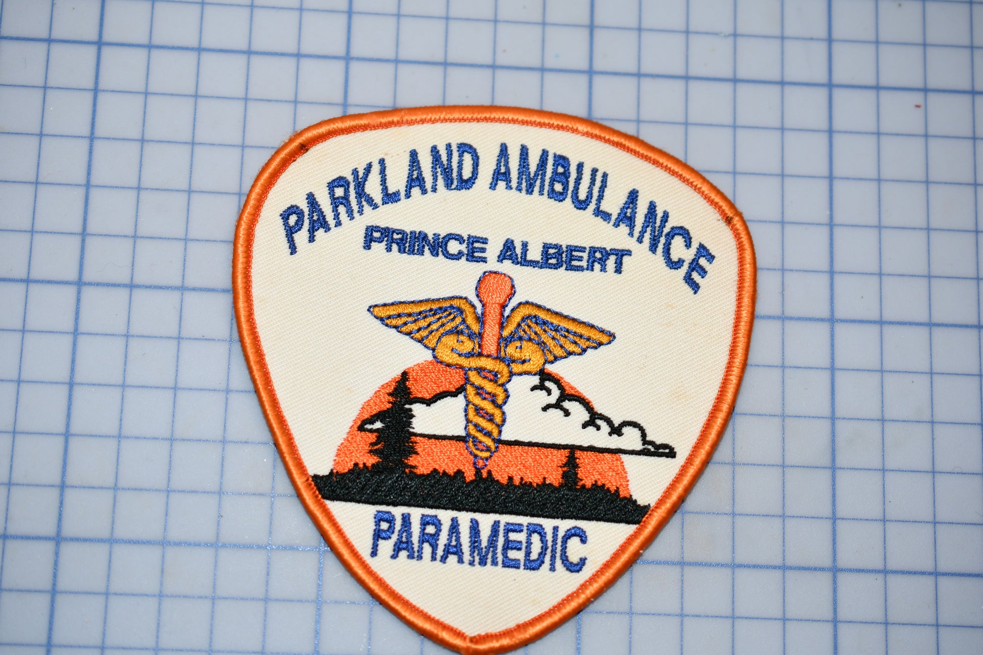 A badge or patch with the text "Parkland Ambulance" and "Prince Albert Paramedic" printed on it, along with an image of a medical symbol.