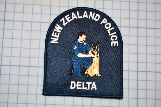 A New Zealand Police Delta police patch featuring a police officer kneeling next to a German Shepherd dog.