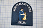 A New Zealand Police Delta police patch featuring a police officer kneeling next to a German Shepherd dog.